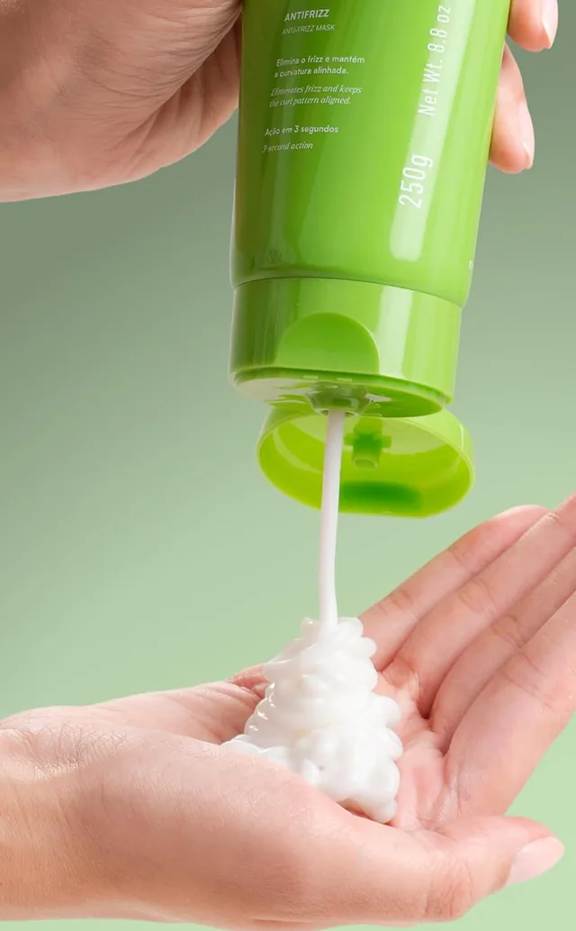 A green Cacho Perfeito tube squeezing white cream into an open palm
